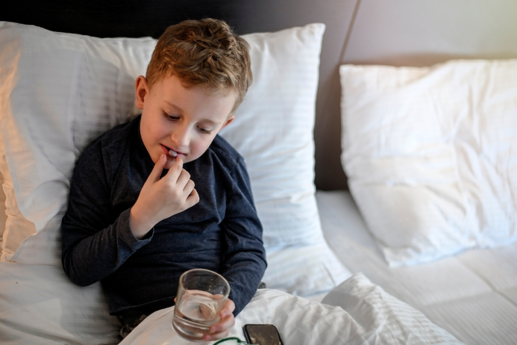 a young boy taking a pill while holding a glass of water